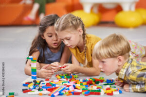 three children lying on floor playing with LEGO style bricks